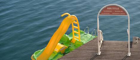 A wooden dock with a yellow and green slide and a shuttle sign indicating nearby locations.