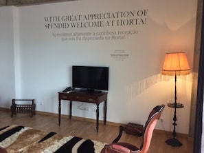 A room with a television on a wooden table, a lamp, and a sign on the wall. - Apartamentos Príncipe Apart-Center (Horta)