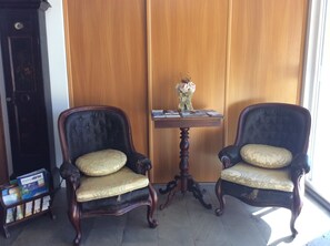 Dos sillones ricamente decorados con asientos acolchados, una mesita de madera con un jarrón de flores y un aparador de madera oscura.