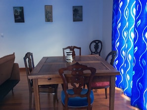 A dining area with a wooden table, chairs, and a blue patterned curtain. - Apartamentos Príncipe Apart-Center (Horta)