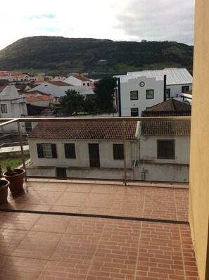 Una terraza con piso de baldosas, un edificio blanco de techo rojo y una colina al fondo.