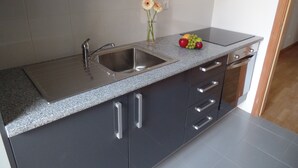 A modern kitchen with a granite countertop, stainless steel sink, and a fruit bowl. - Apartamentos Príncipe Apart-Center (Horta)