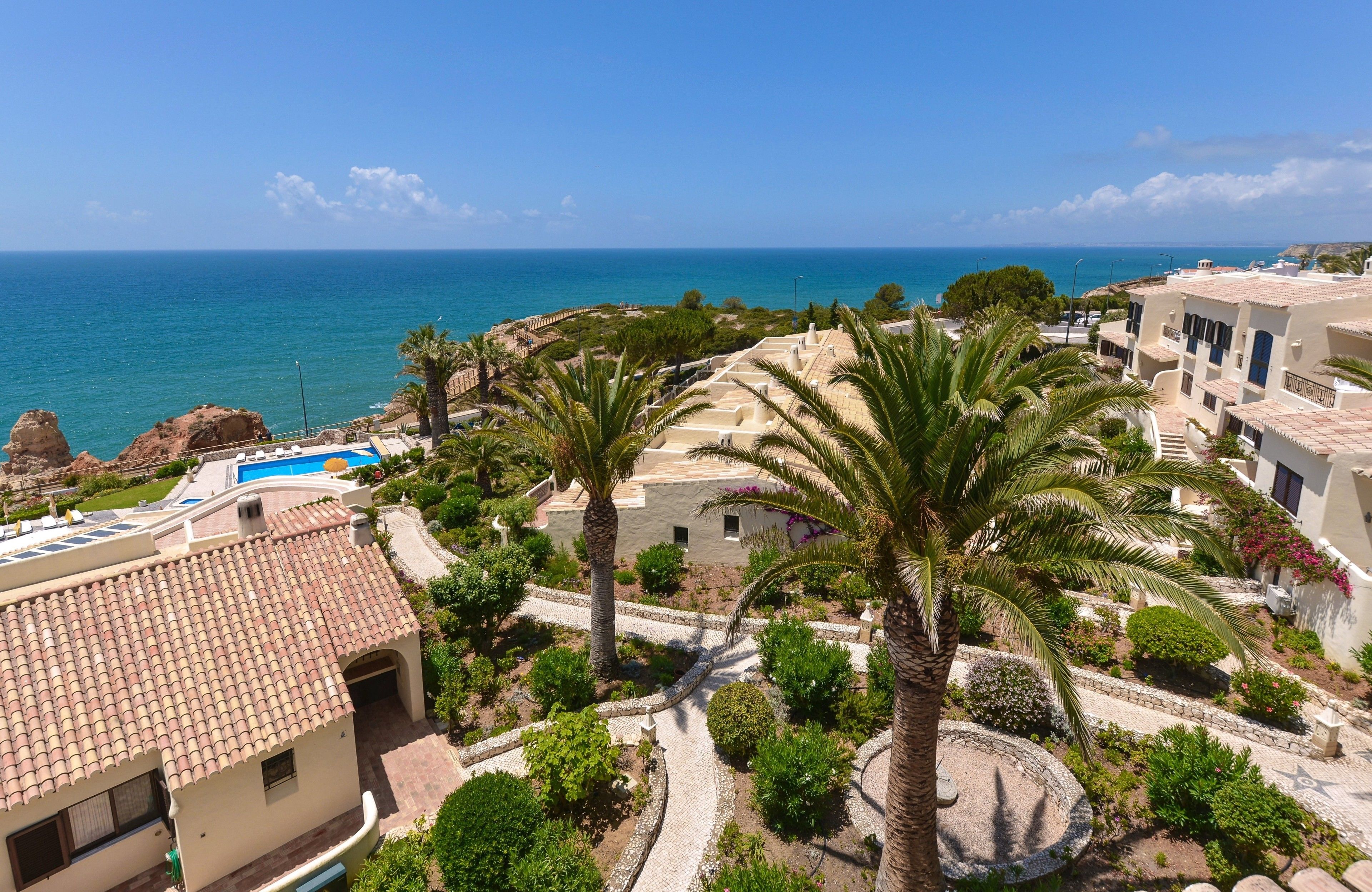 A coastal resort with a swimming pool, palm trees, and a view of the sea.