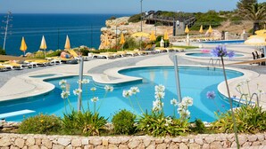 A pool with a unique design, surrounded by sun loungers and umbrellas, with a view of the ocean. - Algar Seco Parque (Lagoa)