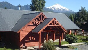 Un edificio de madera rojo con techo inclinado, un porche cubierto y una vista de una montaña nevada al fondo.