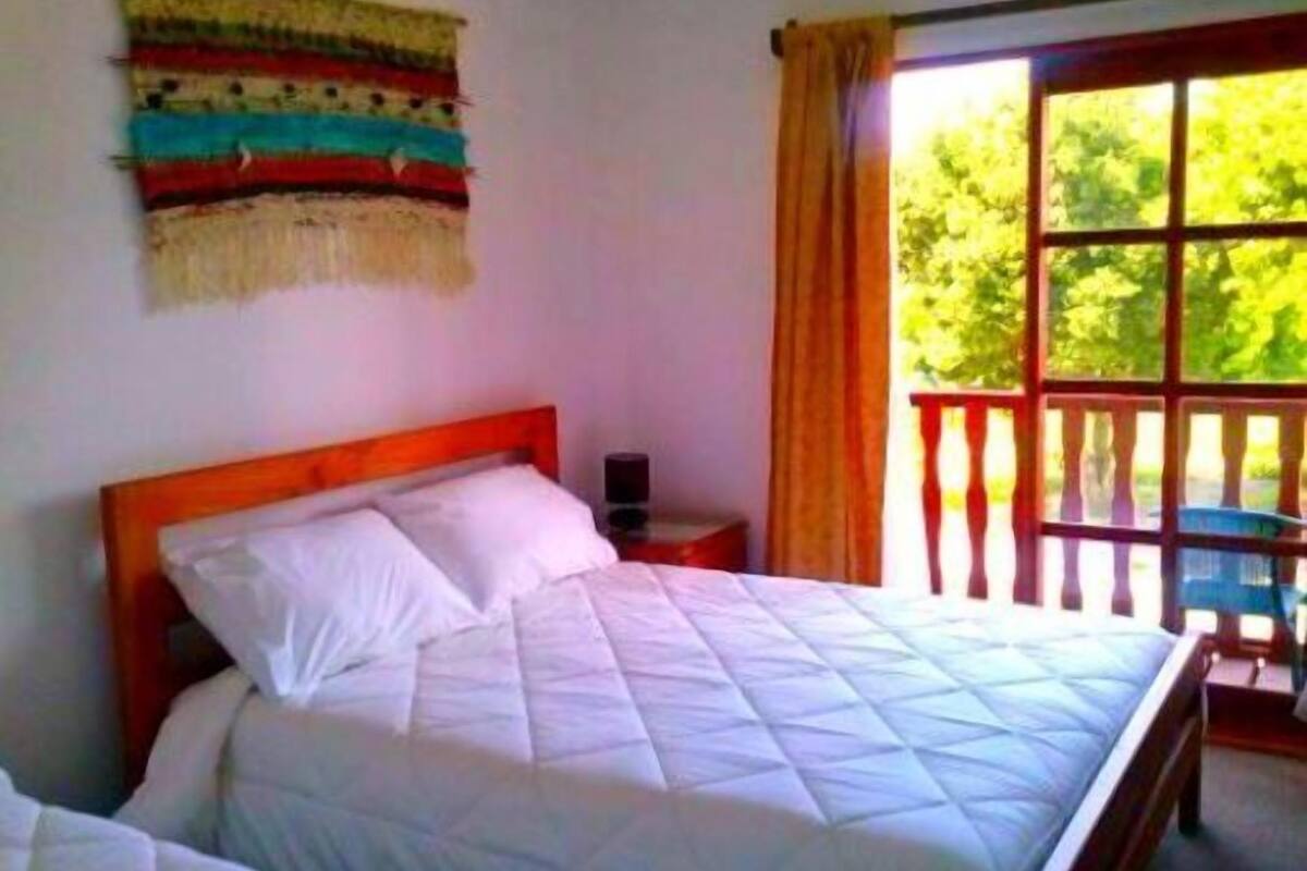 Un dormitorio con una cama, una mesita de noche, una ventana con cortinas y un adorno en la pared.