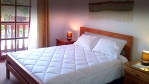 Una cama bien hecha con ropa blanca, un cabecero de madera y una mesita de noche con una lámpara.