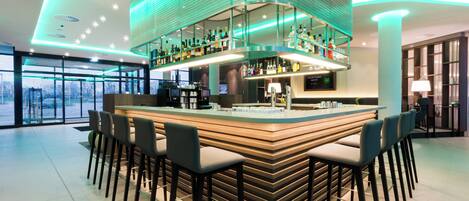 Un espace bar moderne doté d’un îlot central et de nombreux tabourets, d’un plafond haut avec des luminaires encastrés et d’une vue sur l’extérieur grâce à de grandes fenêtres.