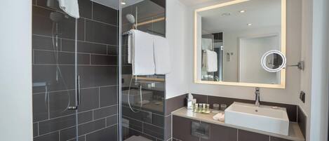 A modern bathroom with a glass-enclosed shower, a large mirror, and a white sink.