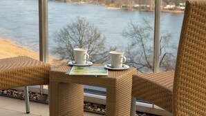 A wicker chair and table with two white cups and saucers, overlooking a river. - Courtyard by Marriott Wolfsburg (Wolfsburg)