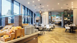 A modern restaurant with a wooden counter, dining tables, and chairs. - Courtyard by Marriott Wolfsburg (Wolfsburg)