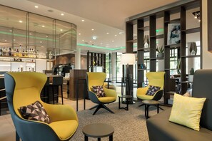 Un espace de détente moderne avec des fauteuils jaunes et noirs, un canapé noir et un bar en arrière-plan.