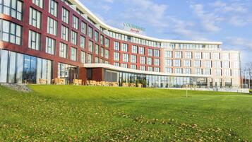 A Courtyard by Marriott hotel with a modern design, featuring a curved facade, large windows, and a grassy lawn in the foreground.