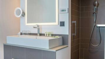 A modern bathroom with a large mirror, a white sink, and a shower area.