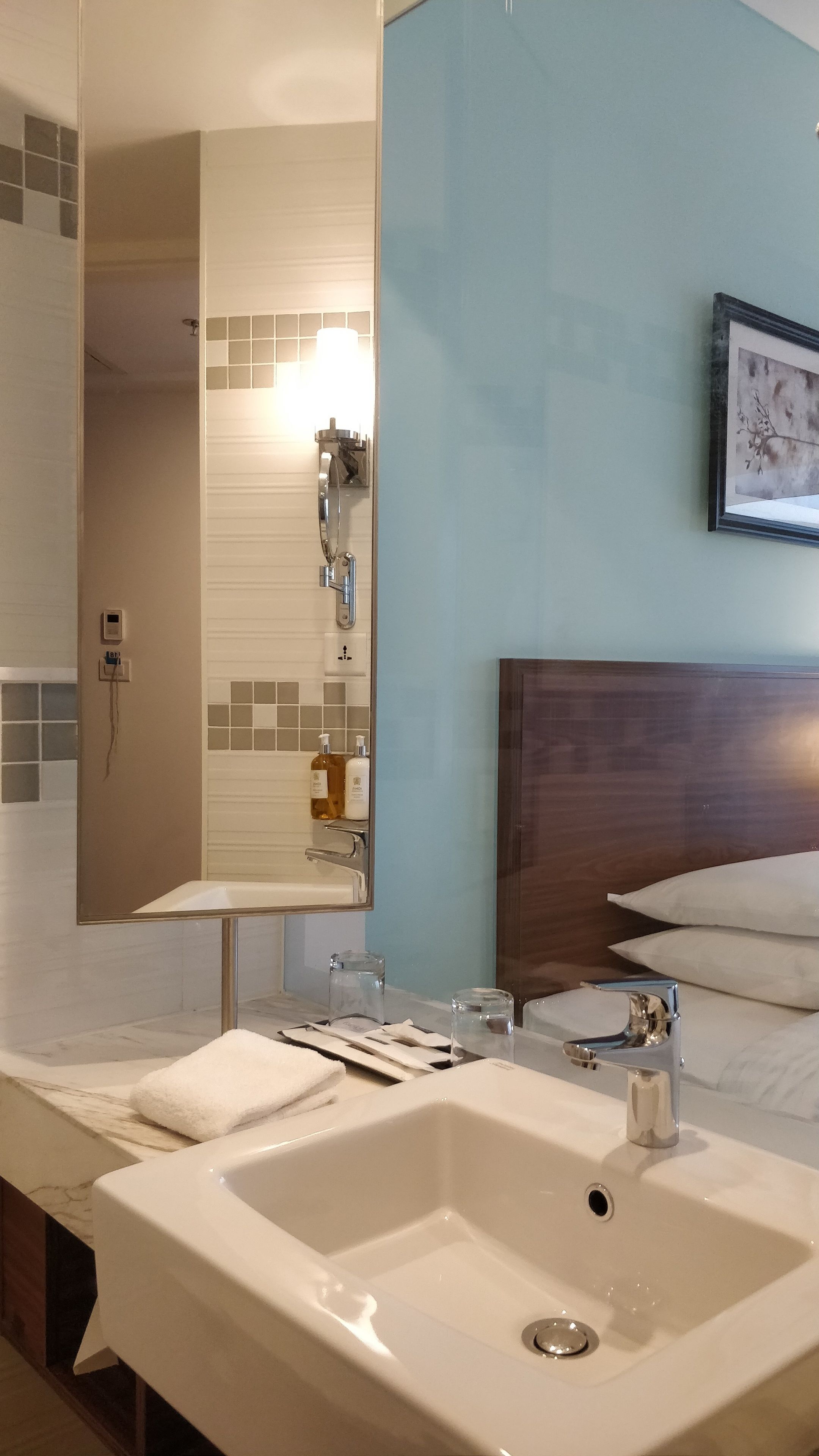 Ein Hotelbadezimmer mit einem großen Waschbecken, einem Spiegel, einer Dusche und einem gerahmten Bild an der Wand.