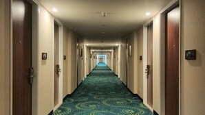 Un pasillo de hotel con alfombra estampada, puertas a ambos lados y una luz al final.