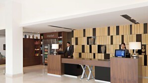 Un moderno mostrador de recepción de hotel con una estación de registro digital, una máquina de café y una pequeña área de cocina.