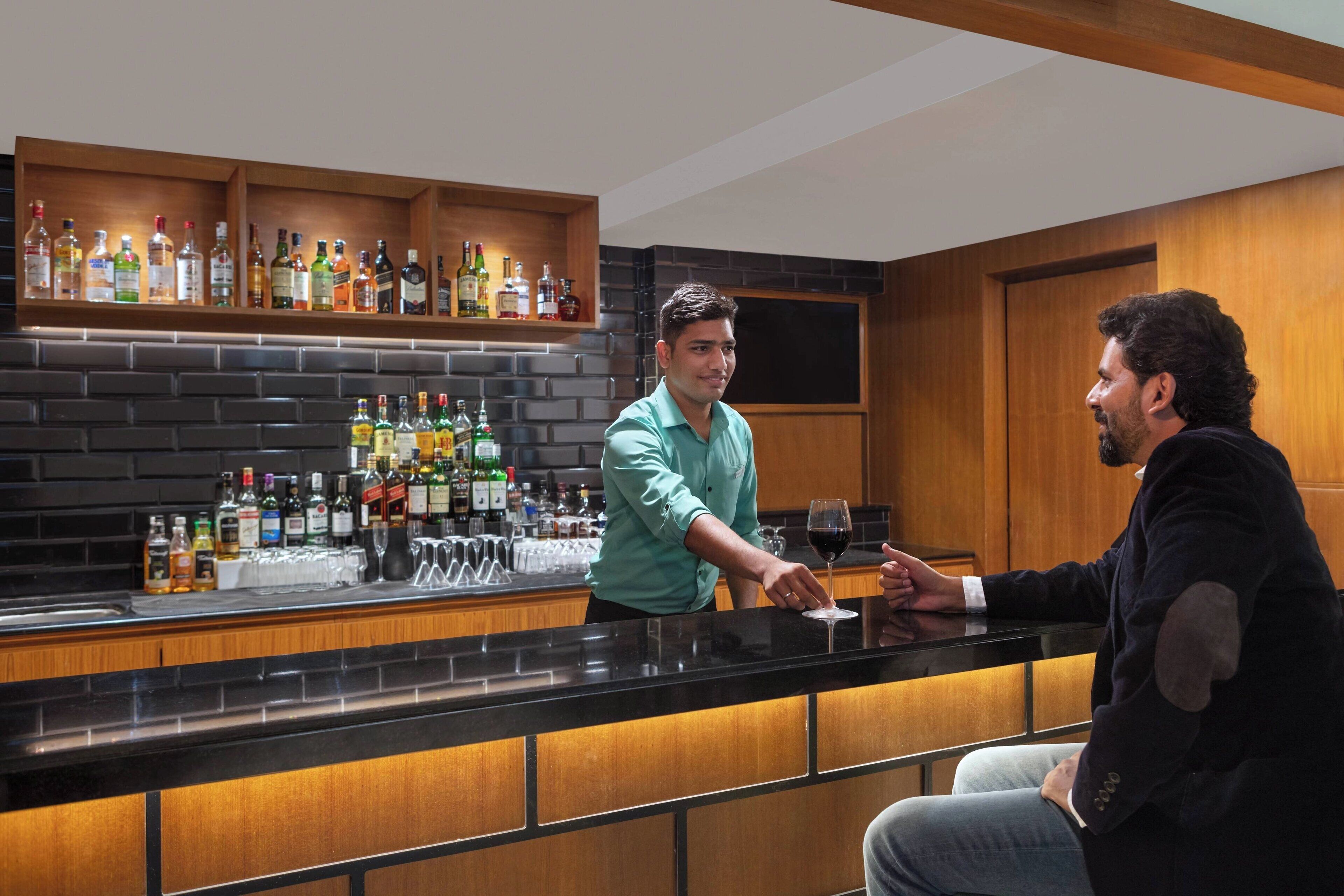 A bar area with a bartender and a customer. There are shelves with various bottles and glasses.