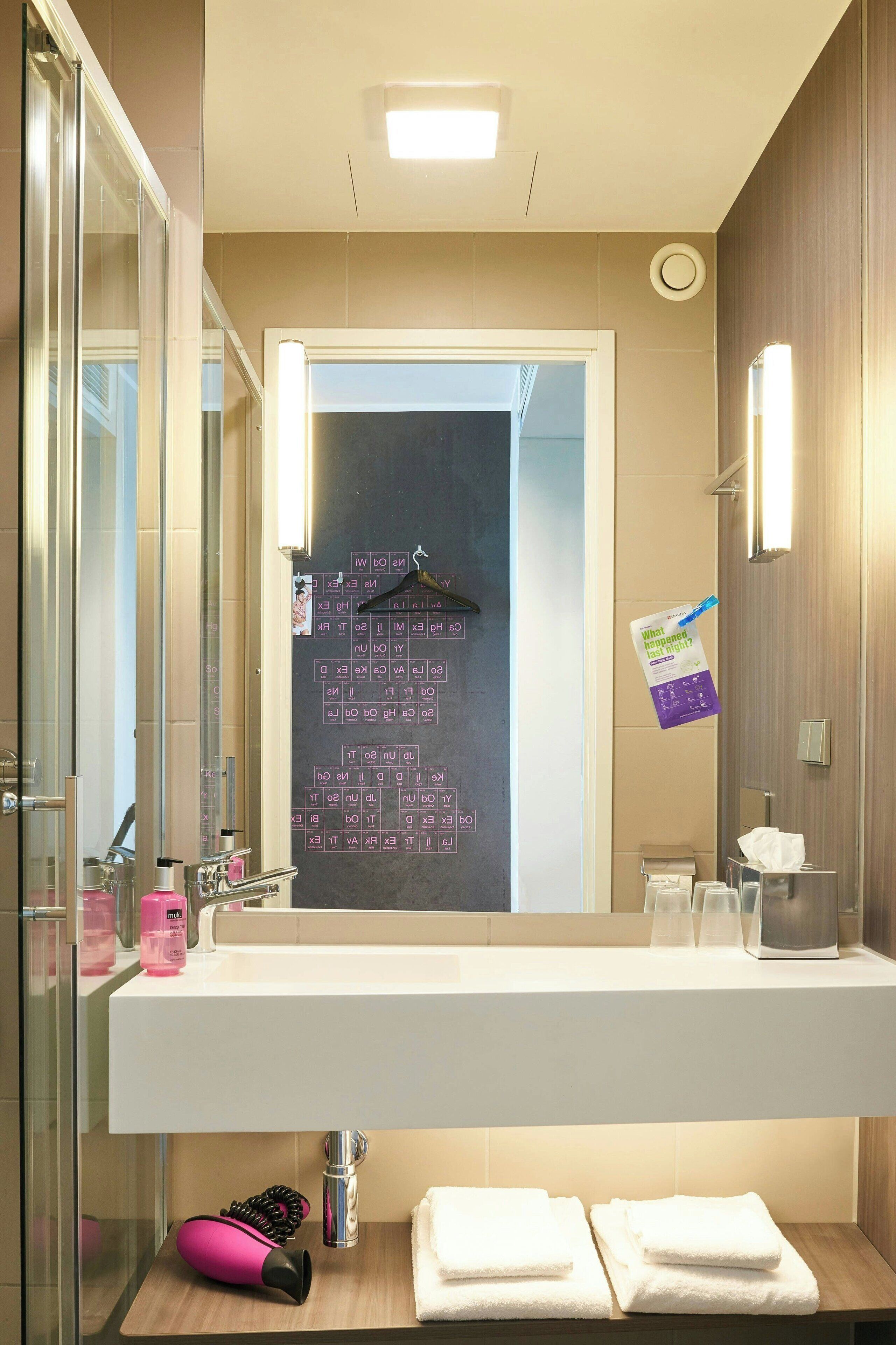 Un baño con un lavamanos blanco, un espejo, un perchero para toallas y un letrero colgado con texto.