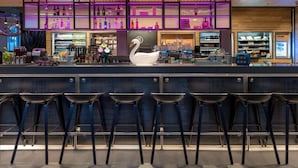 Un espace bar décoré avec un motif de cygne, doté de tabourets de bar, d'étagères remplies de bouteilles et d'un panneau néon.