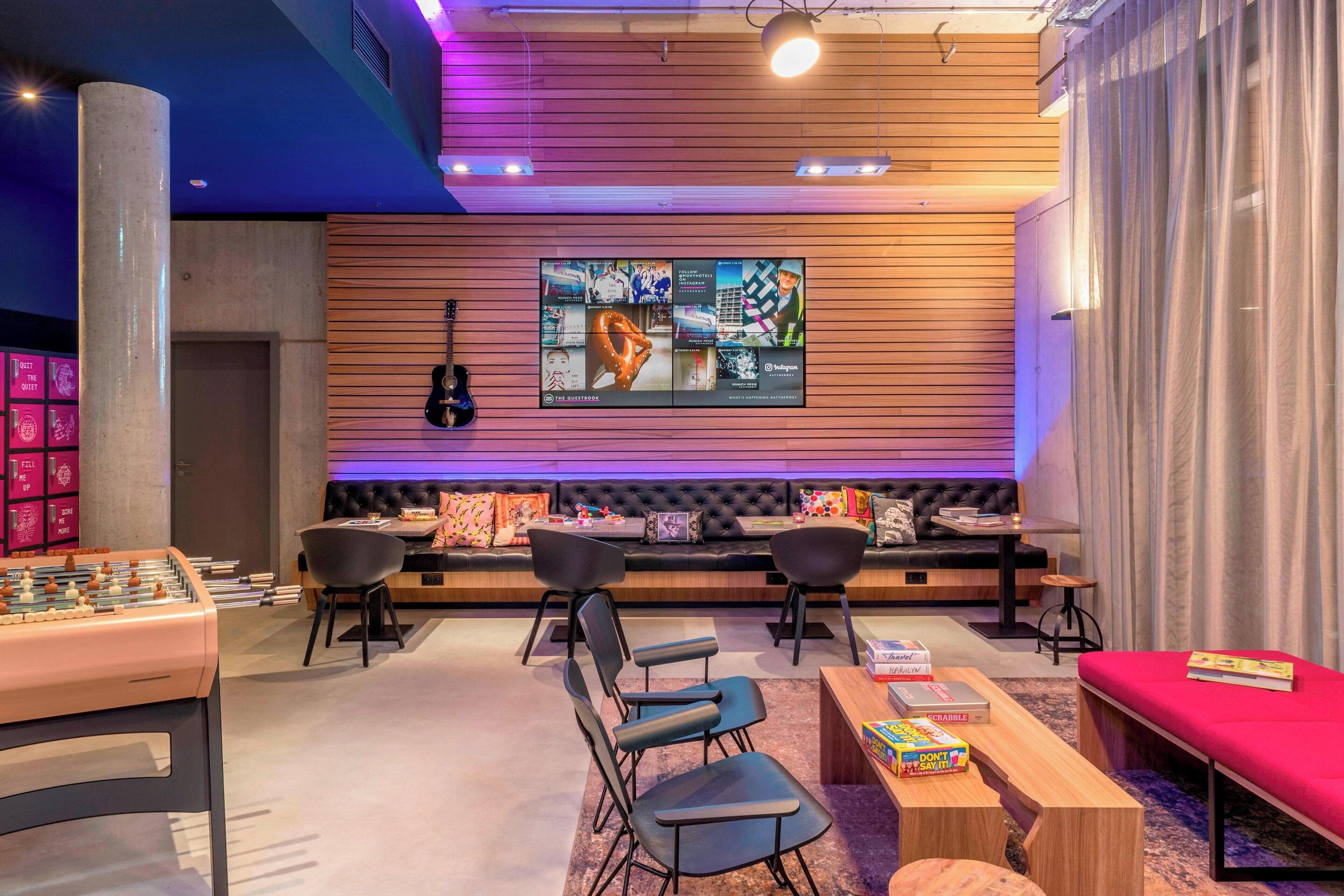 A modern lounge area with a foosball table, comfortable seating, and a large digital screen displaying content.