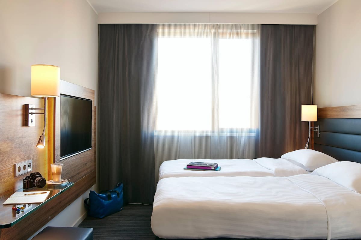 Ein Hotelzimmer mit einem Bett, einem Schreibtisch mit Lampe, einem Fernseher und einem Fenster mit Vorhängen.