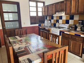 A kitchen with wooden cabinets, a tiled backsplash, a stove, a sink, and a table with a colorful tablecloth. - Villa Serena Centro Histórico (Mazatlán)