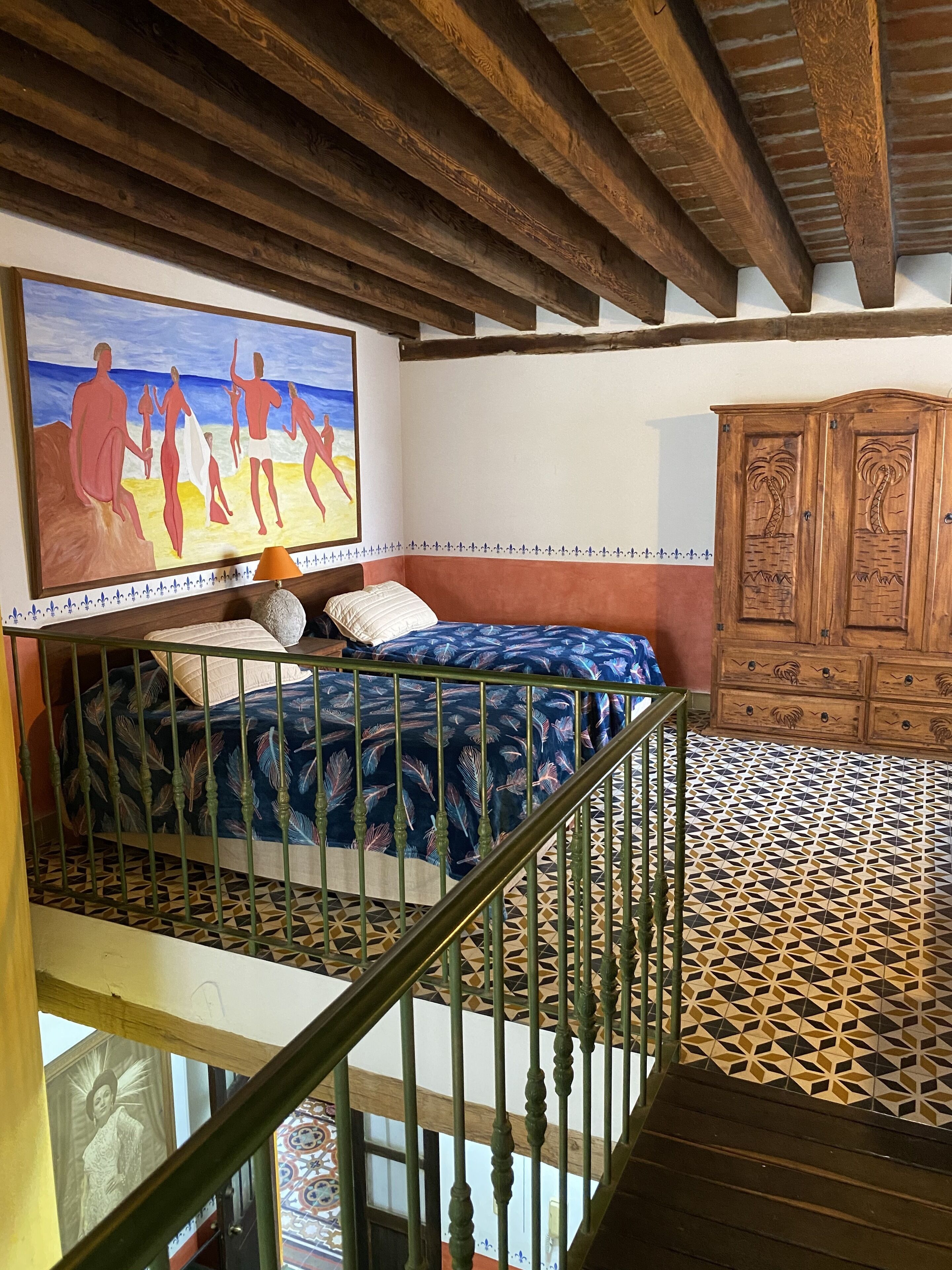 A bedroom with a bed, a painting, a wooden cabinet, and a patterned floor.