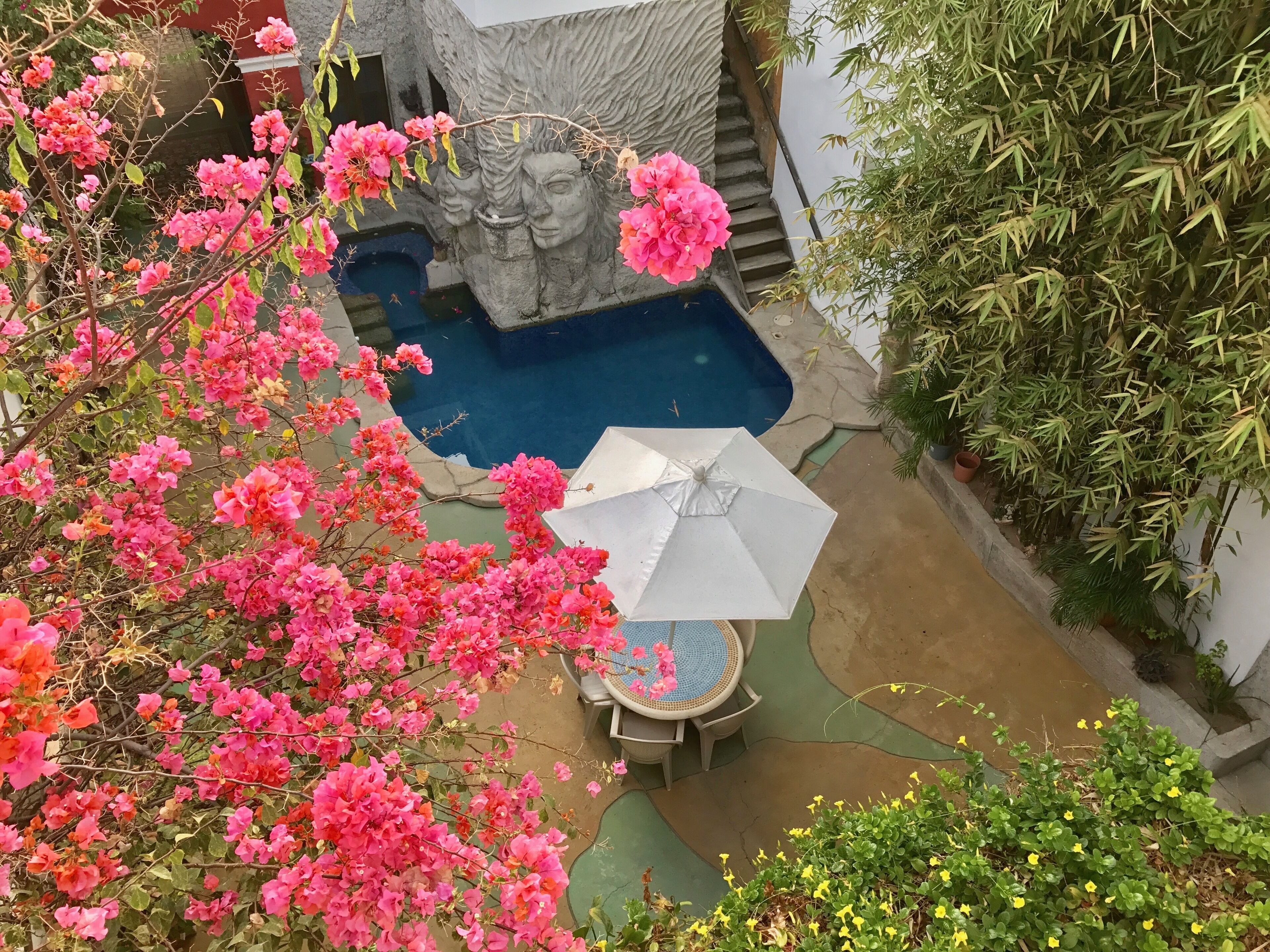 A pool area with a stone sculpture, a table with chairs, and surrounding greenery.