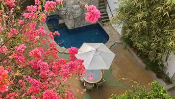 A pool area with a stone sculpture, a table with chairs, and surrounding greenery.