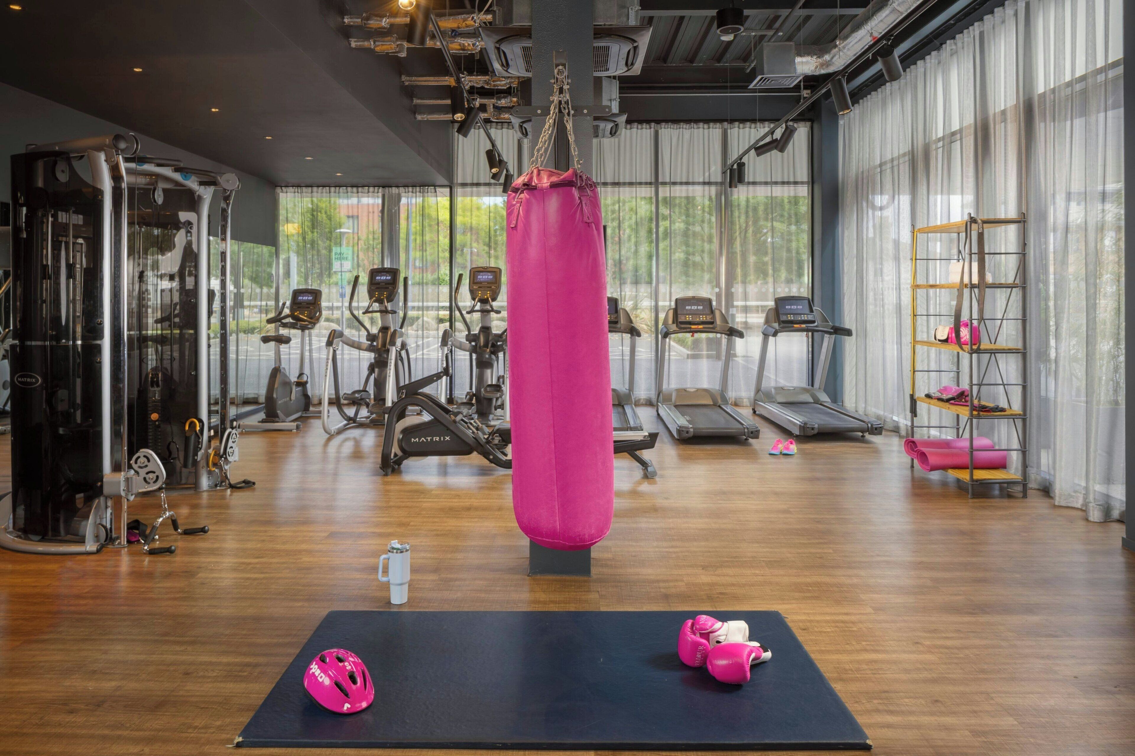 Un gimnasio con máquinas de cardio, un saco de boxeo y colchonetas de ejercicio.