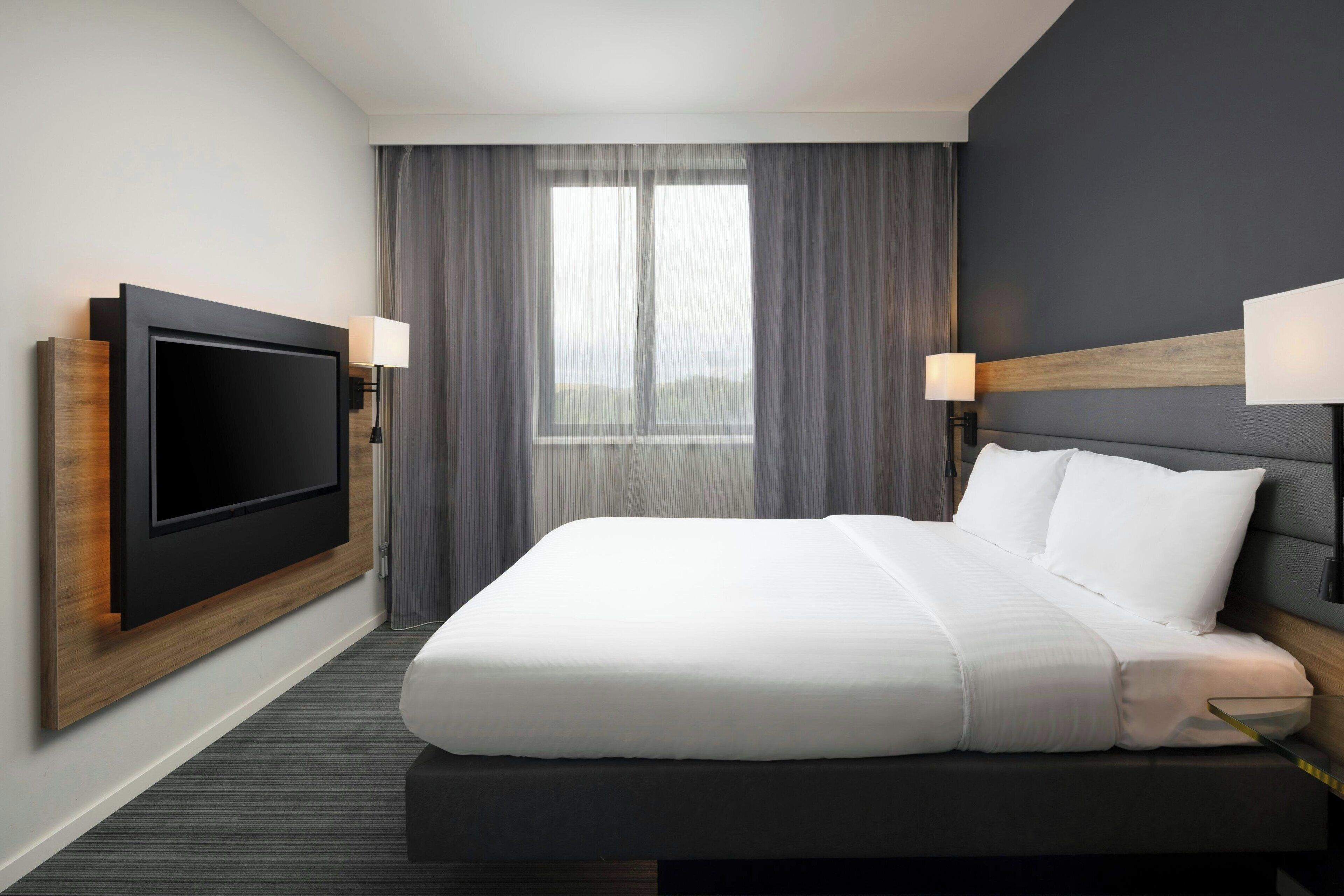 Una habitación de hotel moderna con una cama grande, un televisor de pantalla plana montado en la pared y dos lámparas de noche.