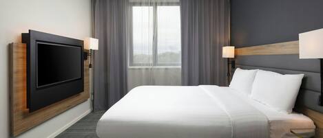 Una habitación de hotel moderna con una cama grande, un televisor de pantalla plana montado en la pared y dos lámparas de noche.