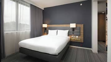 Una habitación de hotel moderna con una cama grande, dos lámparas de noche, un cabecero oscuro y vistas a través de cortinas translúcidas.