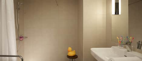 Un baño con ducha, un lavamanos con espejo y un taburete pequeño con un patito de goma.