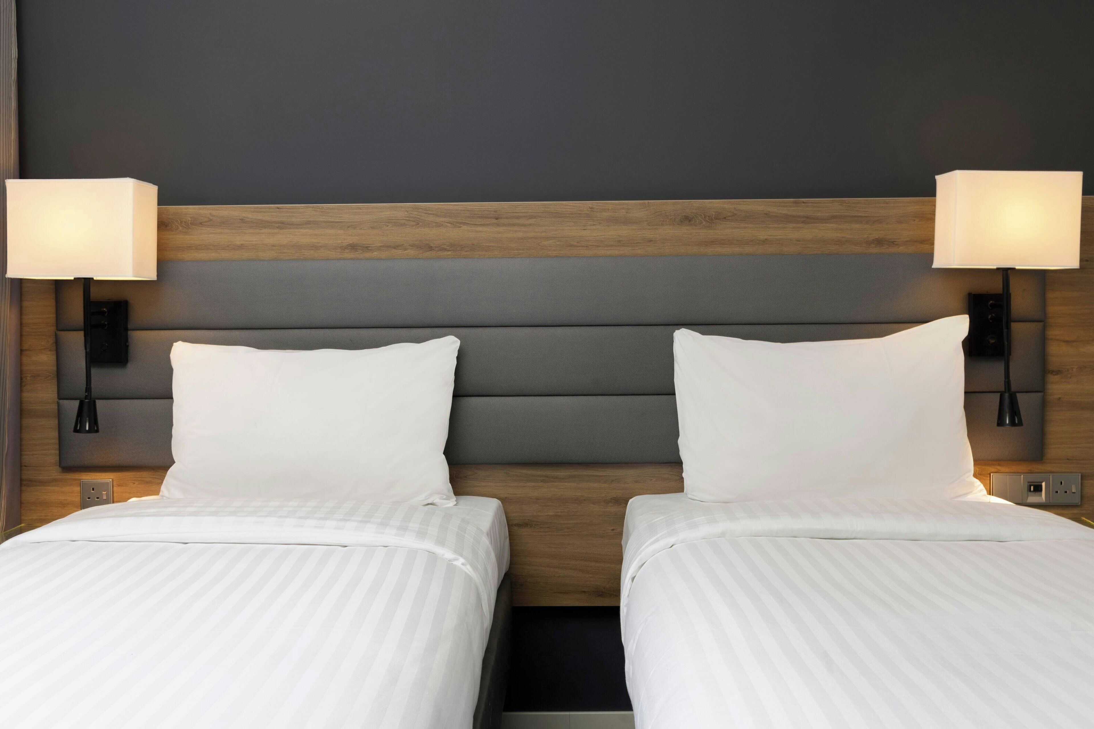 Un lit double avec une tête de lit en bois, deux lampes de chevet et une couleur neutre pour les murs.