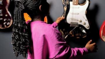Una persona con un vestido rosa de pie frente a guitarras.