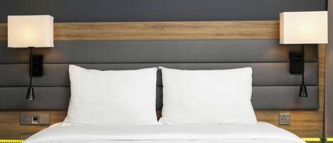 Una cama bien hecha con sábanas blancas, un cabecero de madera y dos lámparas adosadas a las paredes a cada lado.