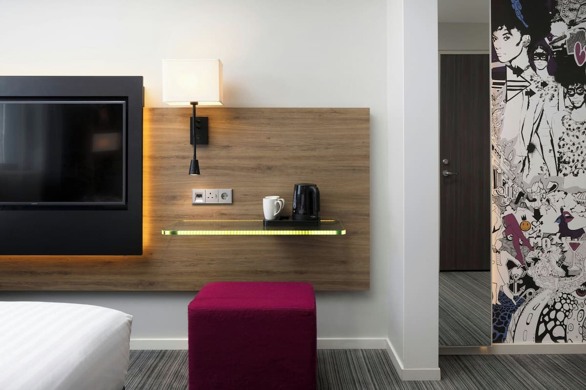 Ein Hotelzimmer mit Fernseher, Nachttisch, Lampe und einer Kaffeemaschine.