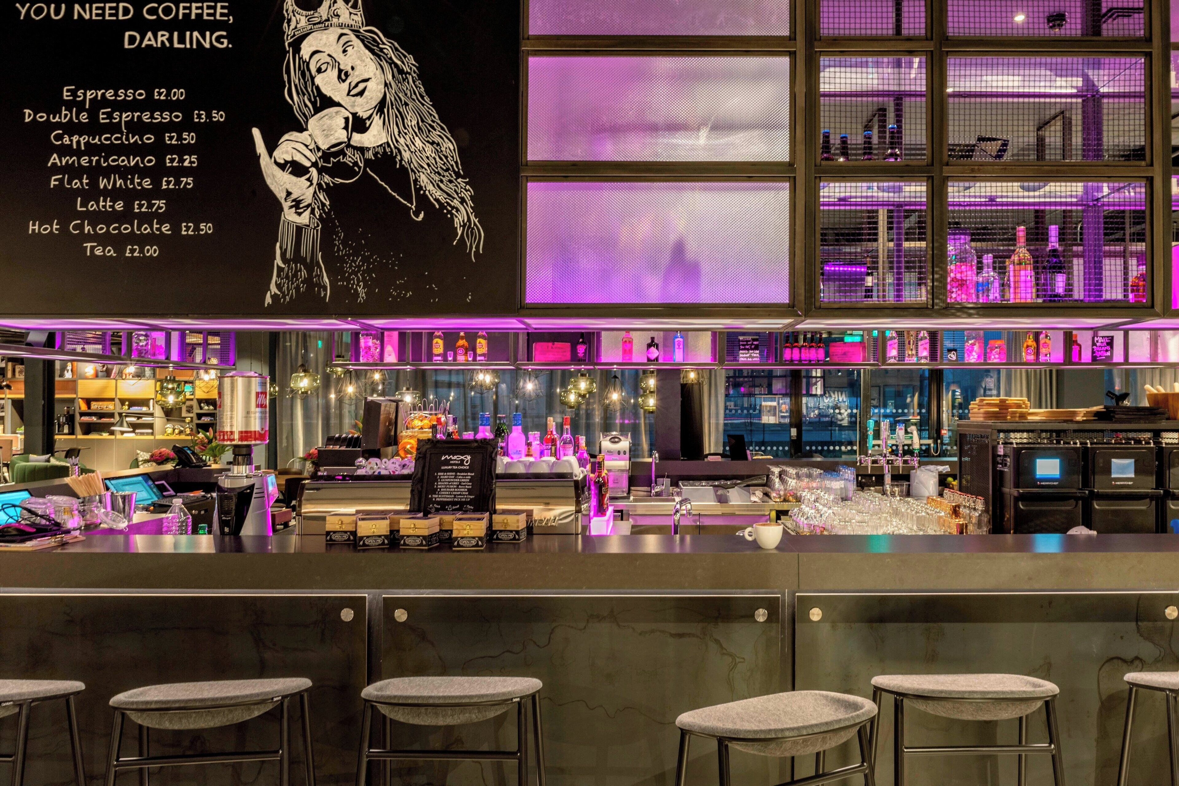 A bar area with a menu board, bar stools, and shelves of bottles.