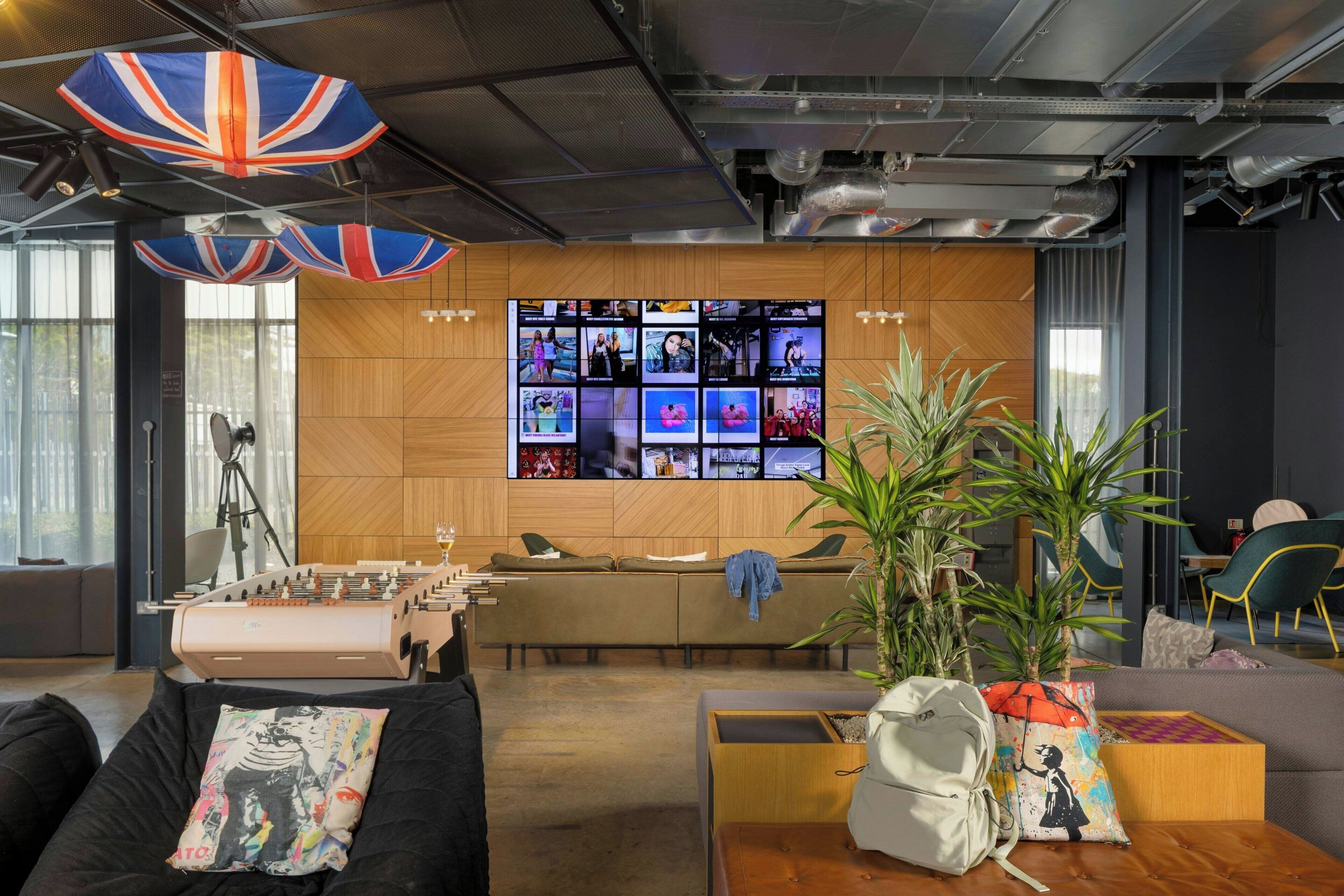Uma área de estar moderna com mesa de futebol, uma grande tela de TV na parede e assentos confortáveis.
