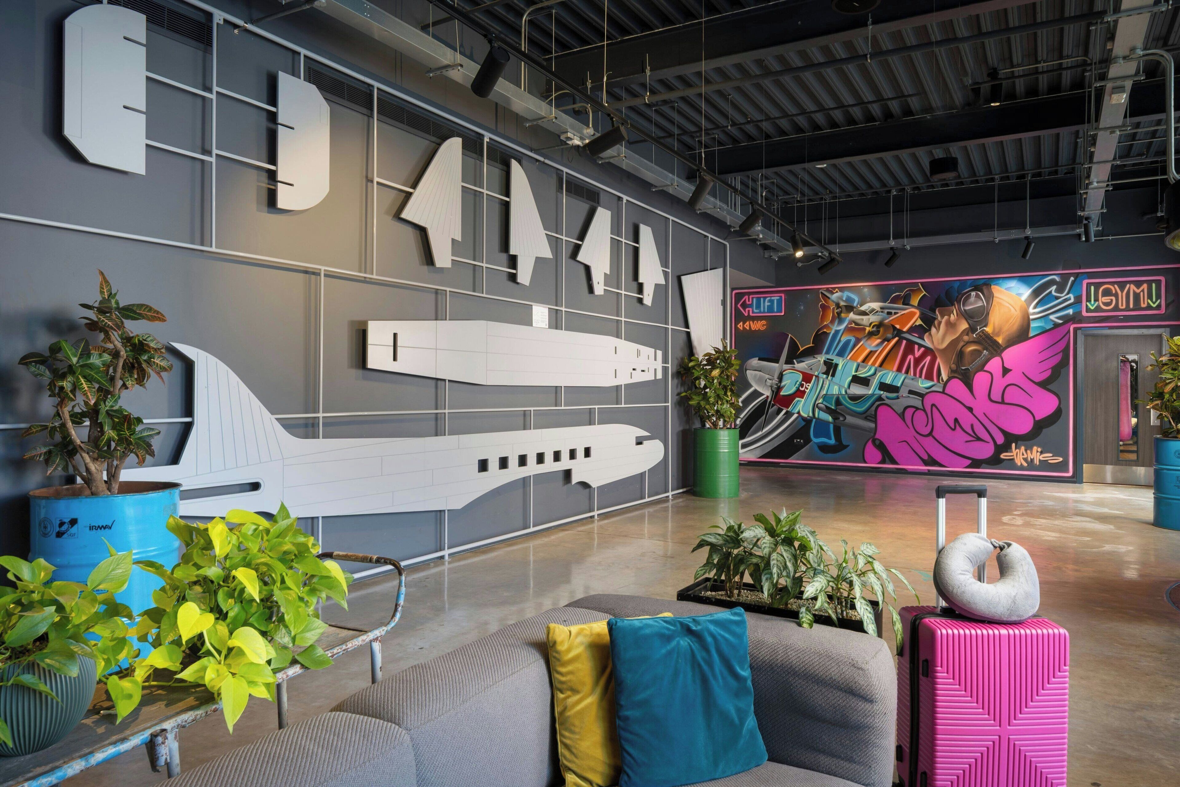 A modern lobby with a large airplane model, potted plants, and a colorful mural.