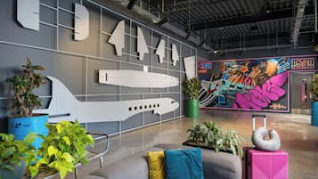 A modern lobby with a large airplane model, potted plants, and a colorful mural.