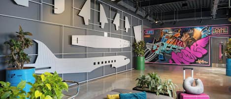 Un vestíbulo moderno con un gran modelo de avión, plantas en macetas y un mural colorido.