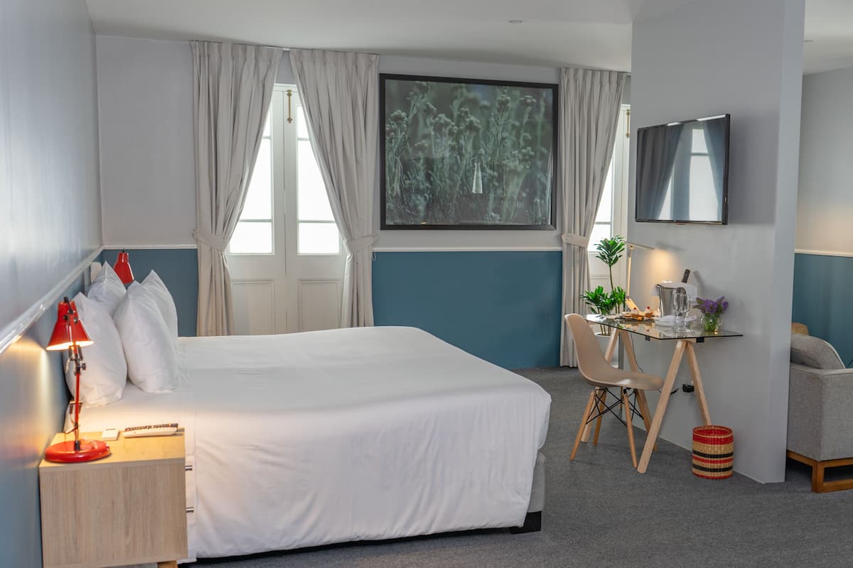 A hotel room with a large bed, a desk with a chair, a TV, and a window with curtains.