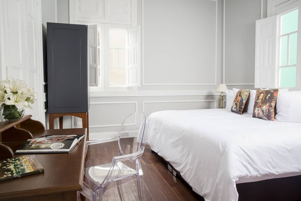 A hotel room with a bed, a desk with a laptop, a chair, and a window with a view.