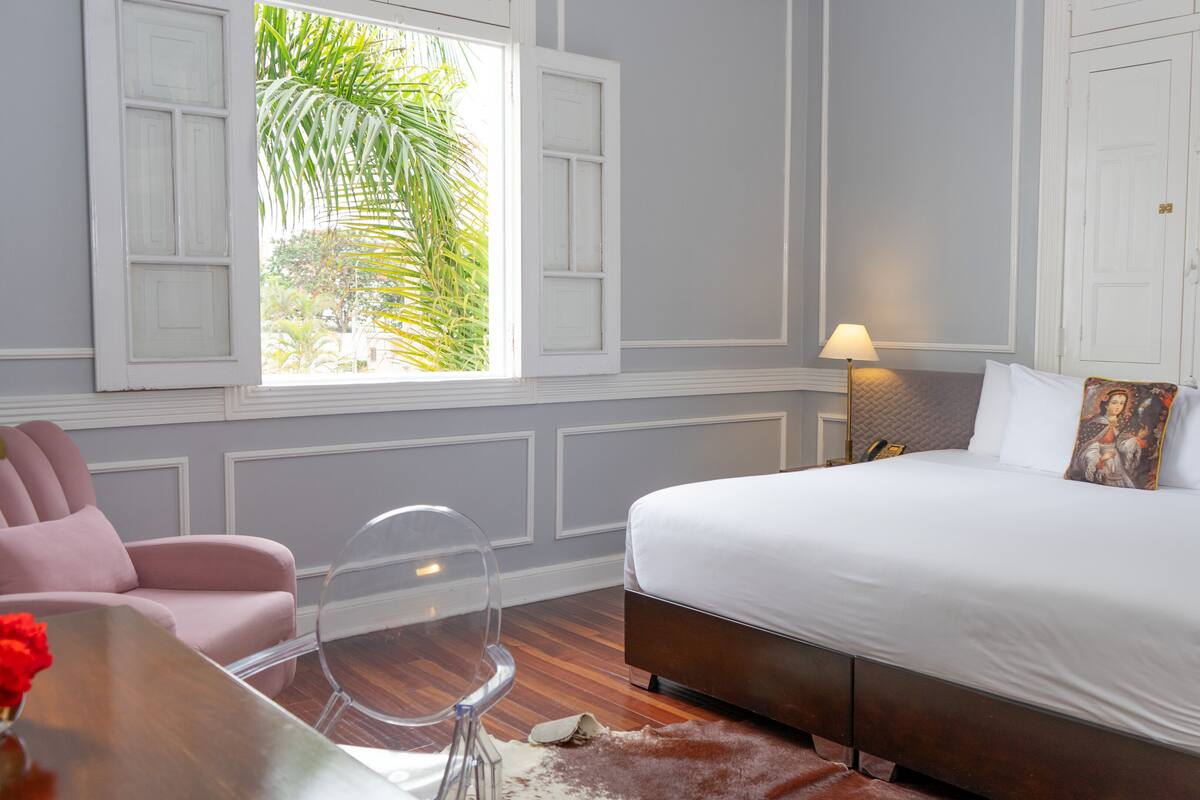 A bedroom with a bed, a chair, a table, and a window with shutters.