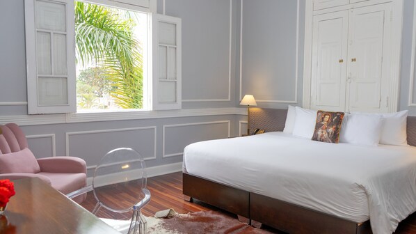 A bedroom with a bed, a chair, a table, and a window with shutters.