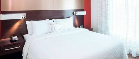 Habitación de hotel con una cama grande, cabecero de madera, mesita de noche con un teléfono y mesita auxiliar.