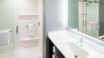 Un baño moderno con ducha de vidrio, un lavamanos blanco y un espejo grande.